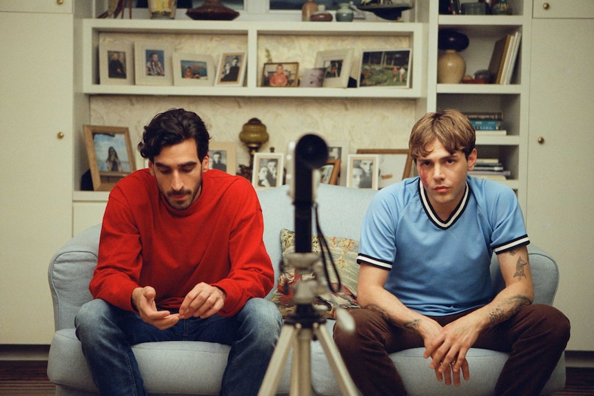 A still from Matthias and Maxime with two young men sitting on a couch in front of a tripod