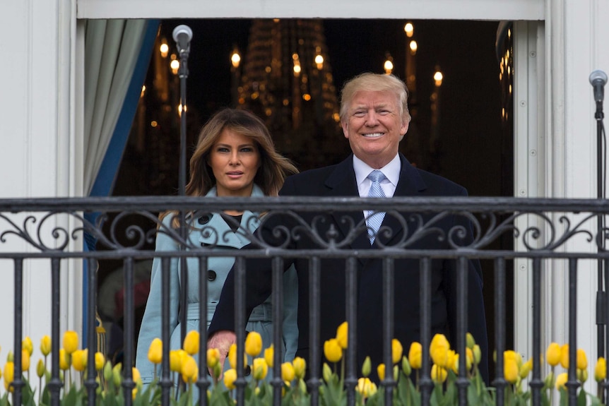 Wide shot of a woman and a man standing on a balcony facing outside.