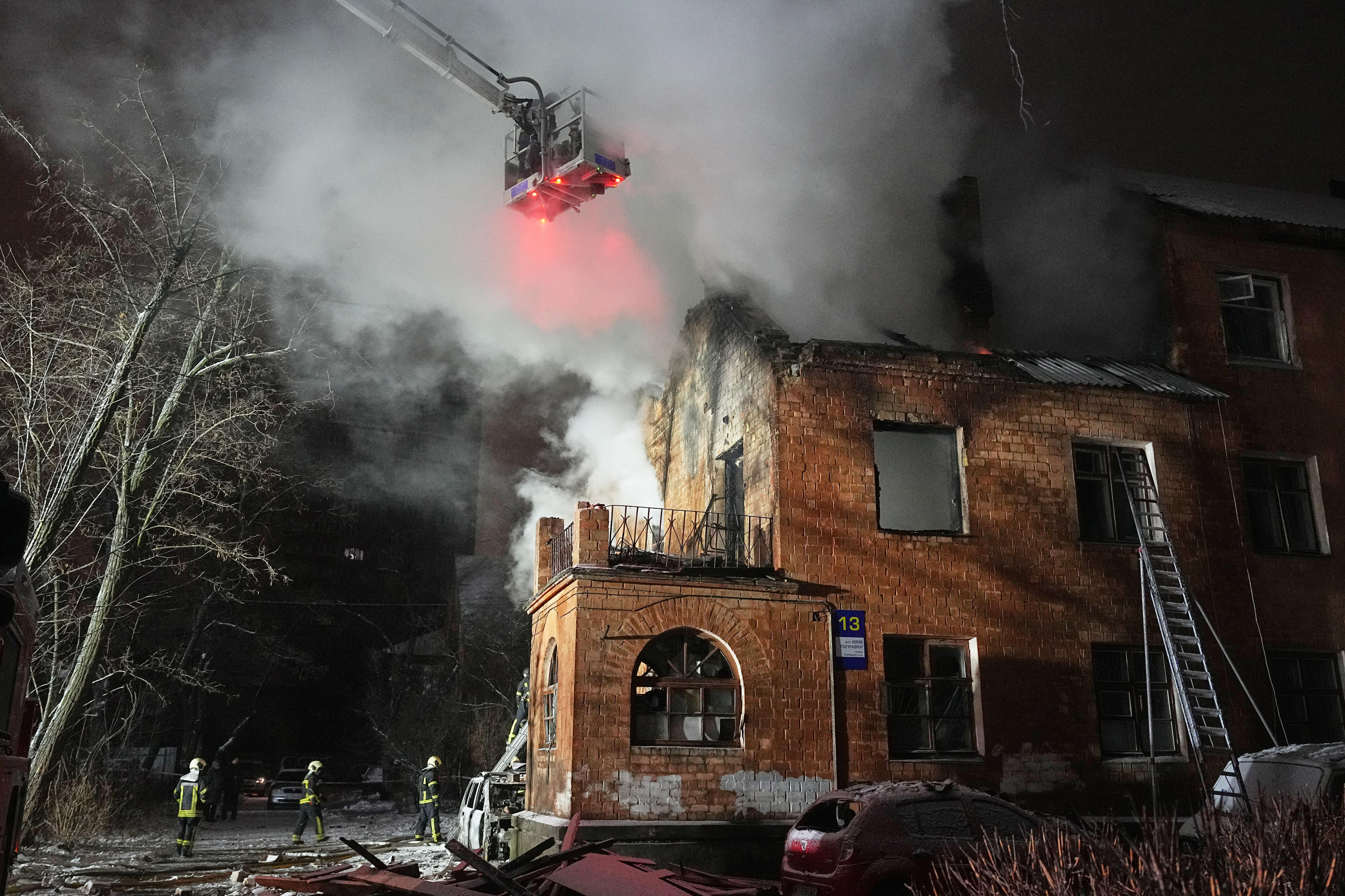 Rescue workers are using ladders and cranes to put out a fire in the roof of a residential building.