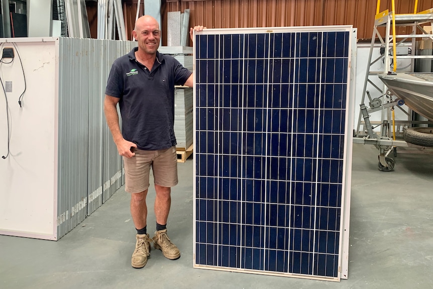 A man stands next to an upright solar panel in a storage shed.