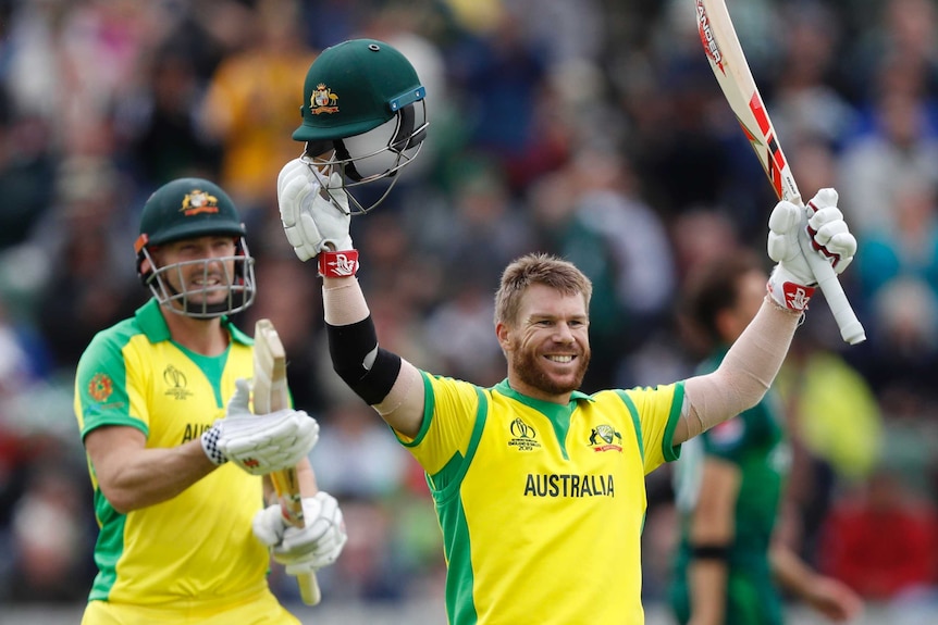 David Warner holds his bat and helmet aloft and smiles broadly. Behind him, Shaun Marsh smiles and applauds.