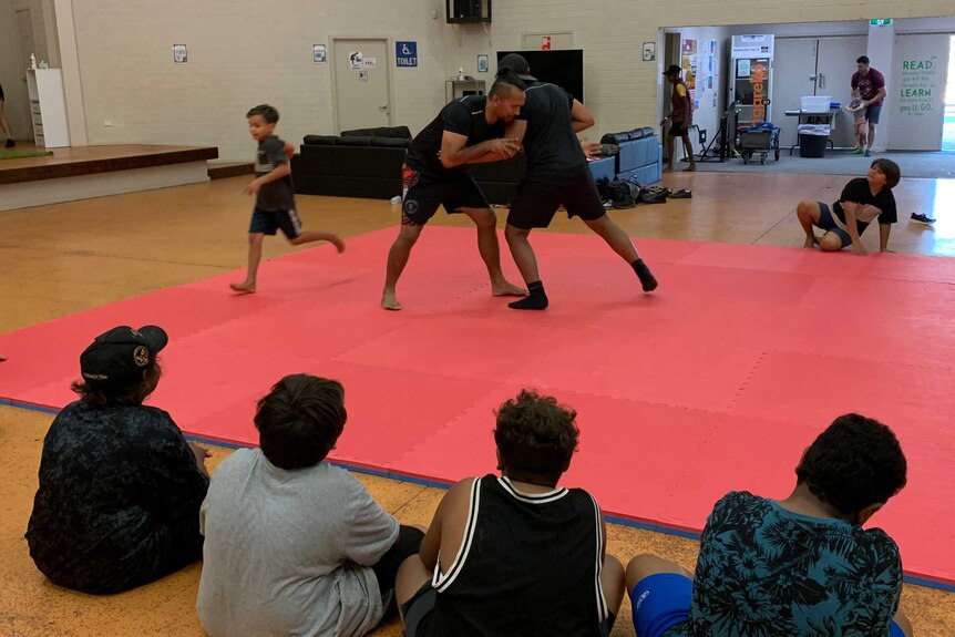 A teacher and student practising wrestling techniques while other kids watch on