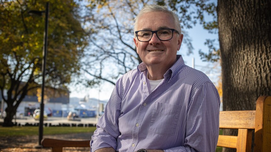 Andrew Wilkie smiles at the camera while sitting on a park bench.