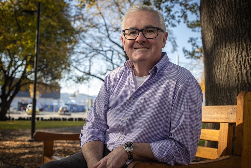 Andrew Wilkie smiles at the camera while sitting on a park bench.