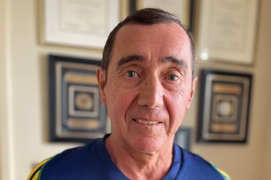 A man in headshot with framed awards on a wall beind him.