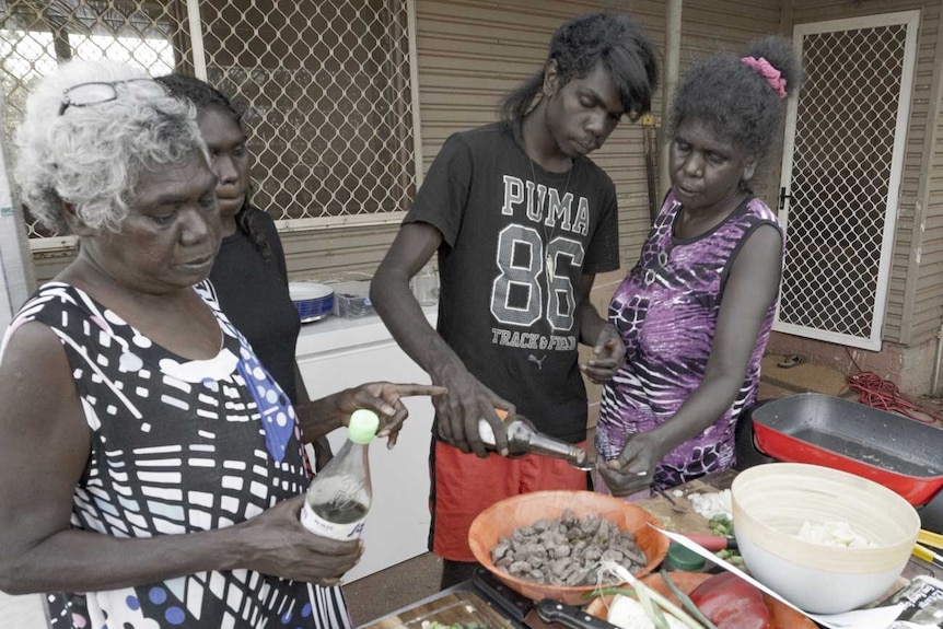 Three women teaching a fourth man how to cook