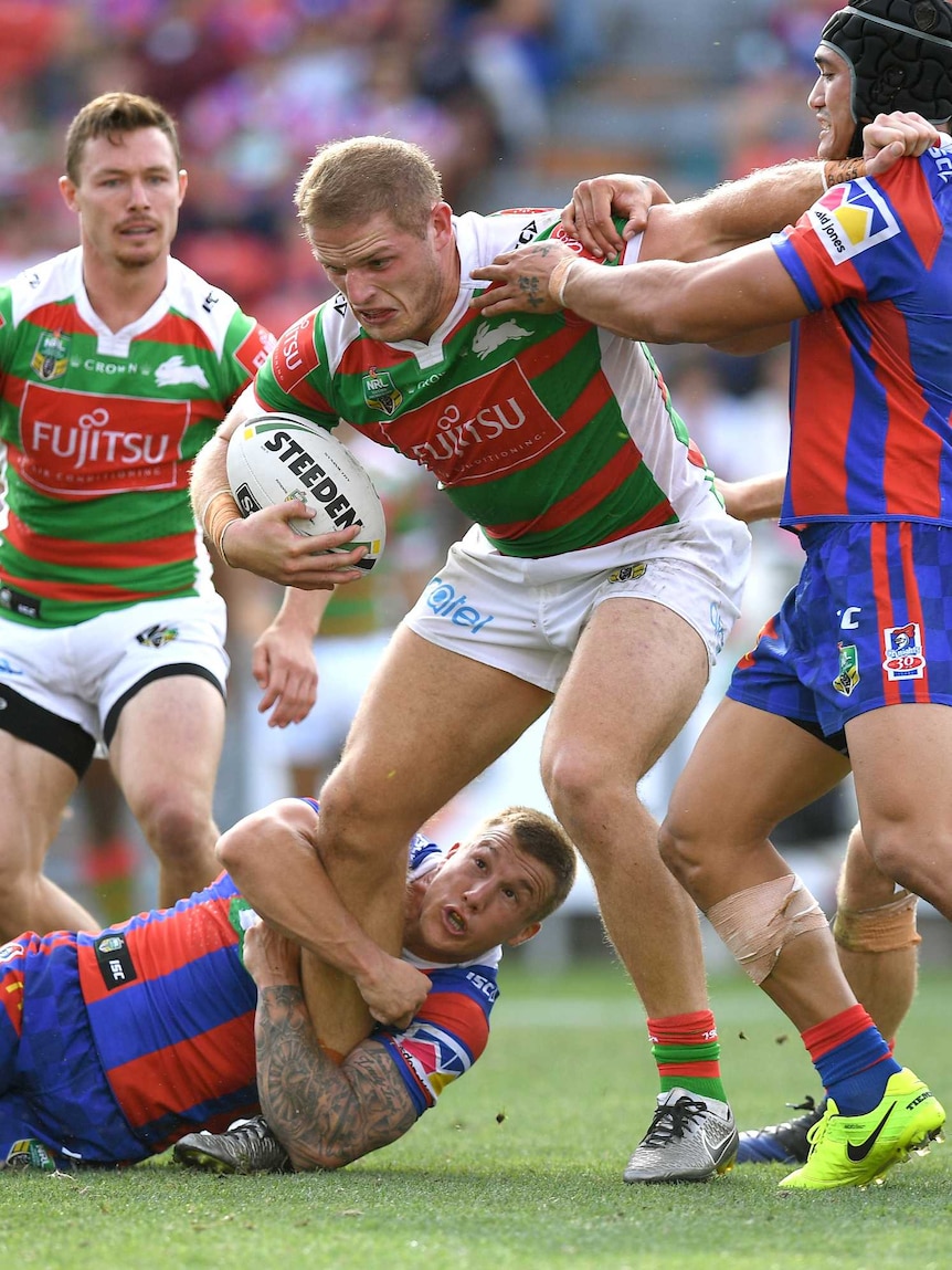A man with a green and red top is wrestled by other footballers