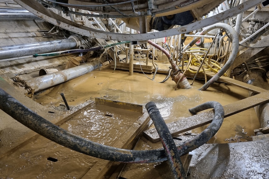 Assorted pipes, hoses and machinery with an amount of muddy water at their base. 