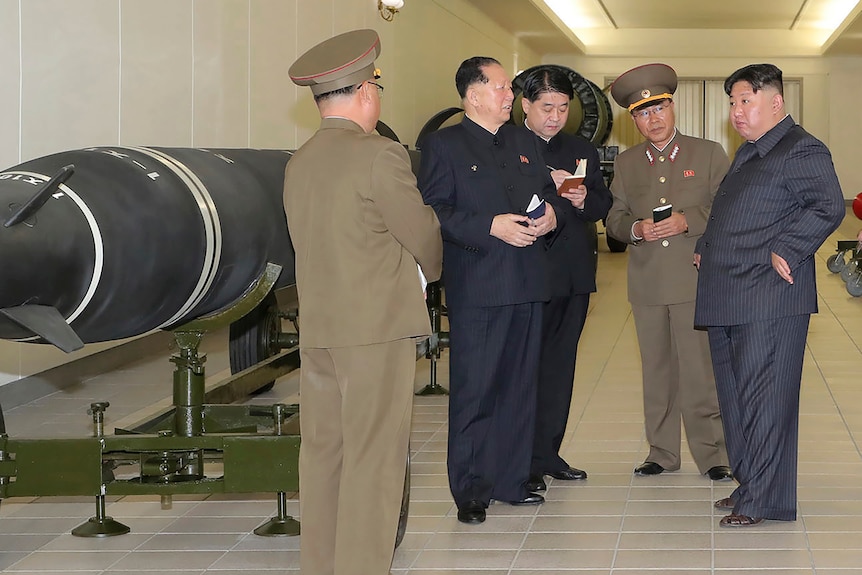 Kim Jong Un speaks to three North Korea officials in a hall displaying different warheads