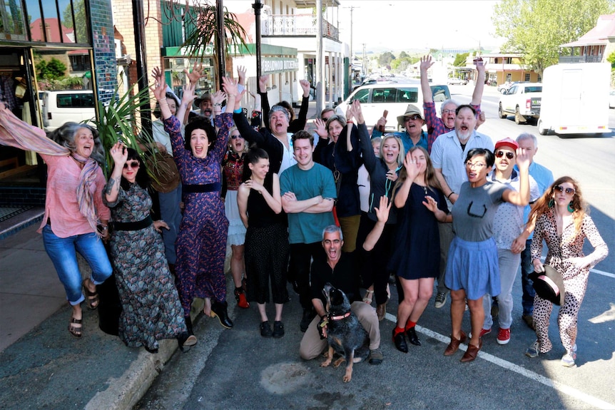 A group of Braidwood residents in colourful clothing jump up, looking happy.