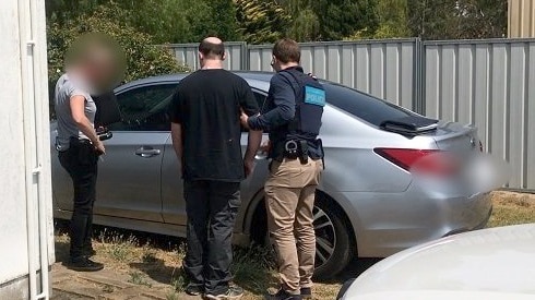 Two police officers escort a balding man to an unmarked police vehicle.