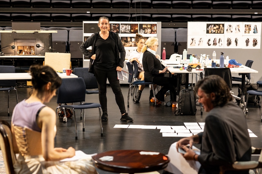 Lee Lewis, a middle-aged white woman with dark hair, wears all black and directs actors in a rehearsal room.