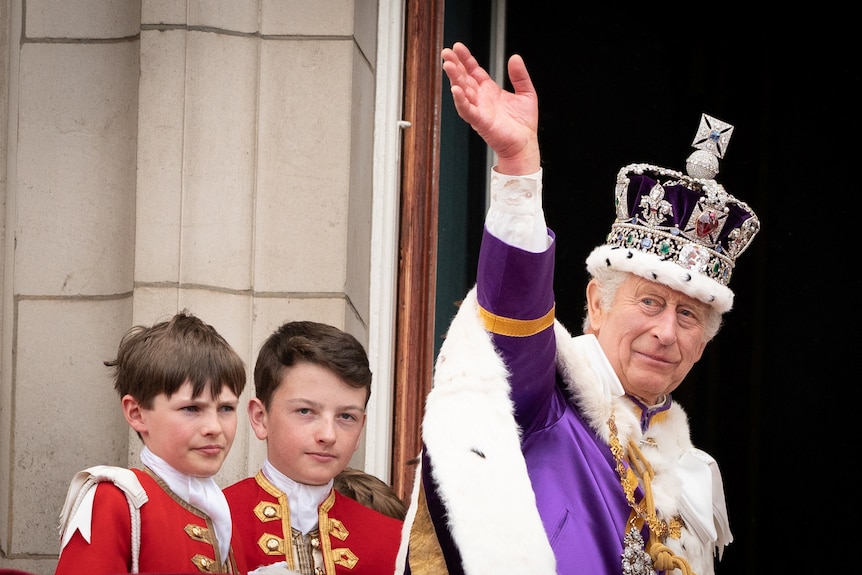 King Charles waves wearing a crown and a purple and white robe.