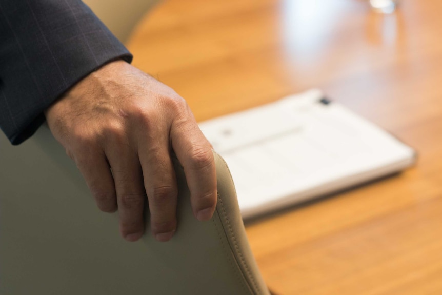 A man's hand reaches for a boardroom chair.