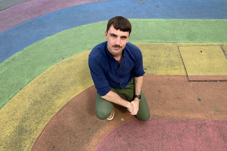 A man kneeing near a rainbow flag.