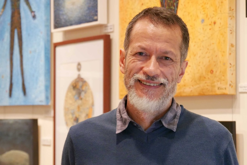 Male artist, Beric Henderson, standing in front of paintings in an art studio.