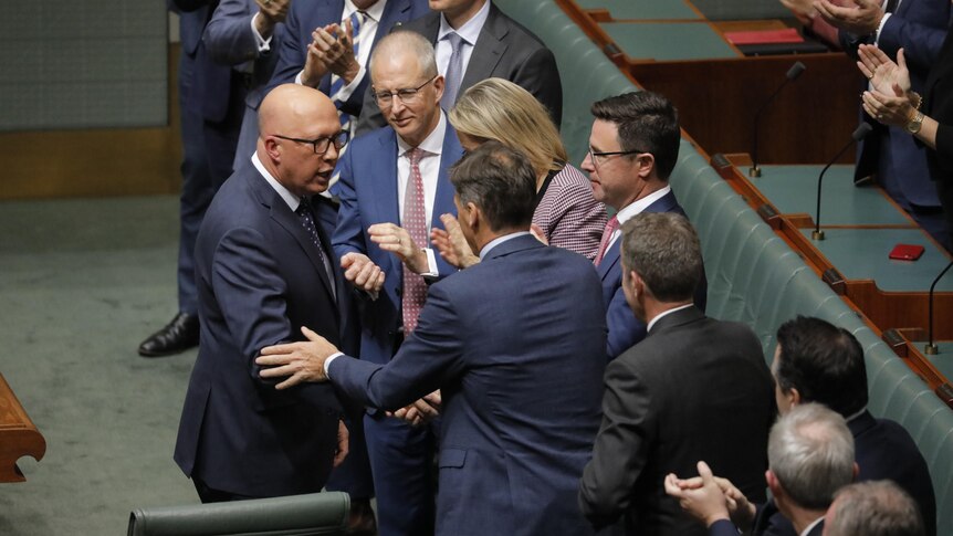 Dutton shakes hands with someone, while others applaud him, on the floor of the House of Representatives.