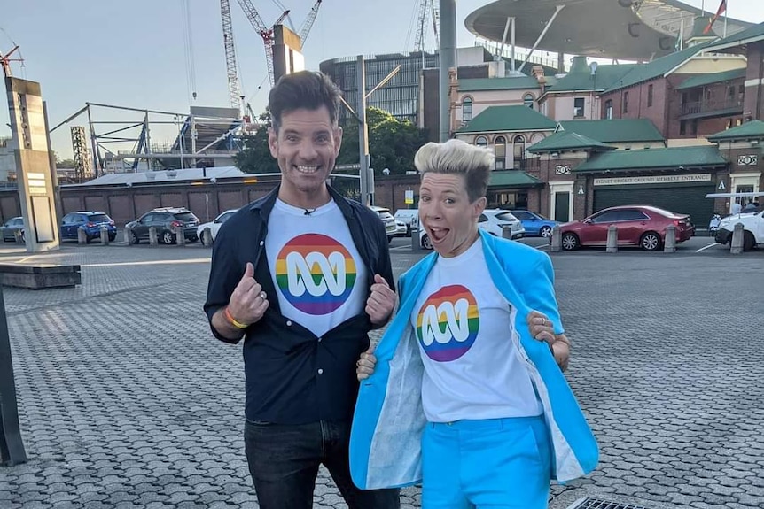 Man and woman standing next to each other wearing tshirts under their shirts that have ABC rainbow logo.