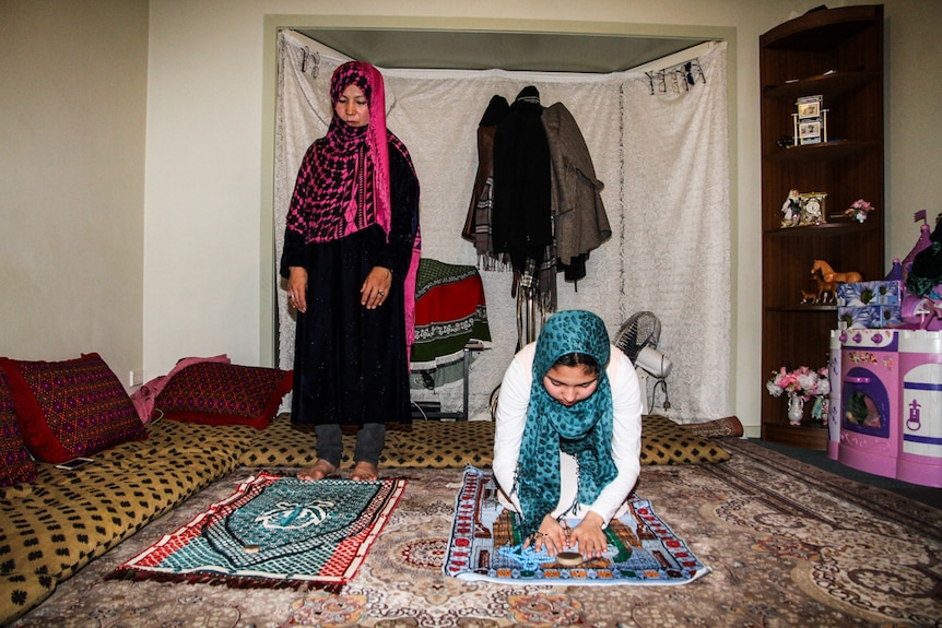 two women praying on mats on the floor in their home