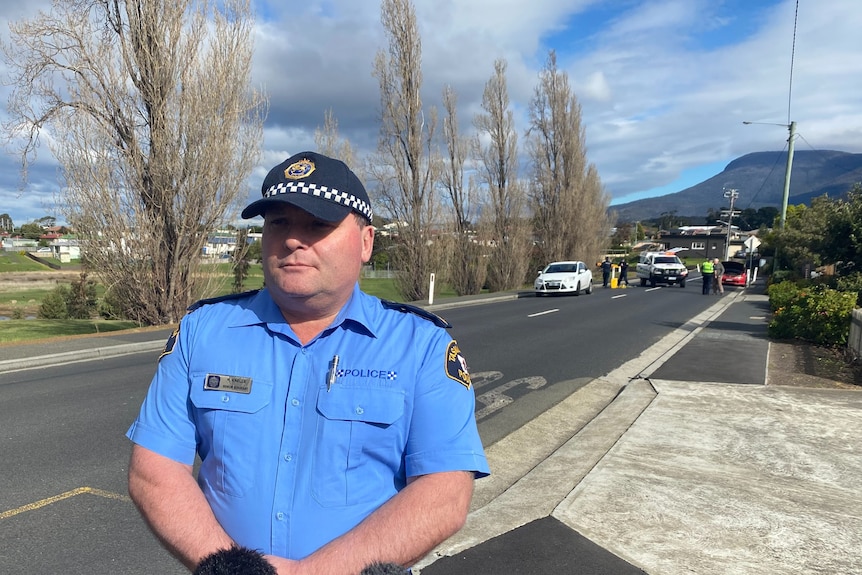 Tasmanian police officer in uniform stands by the side of a vehicle accident