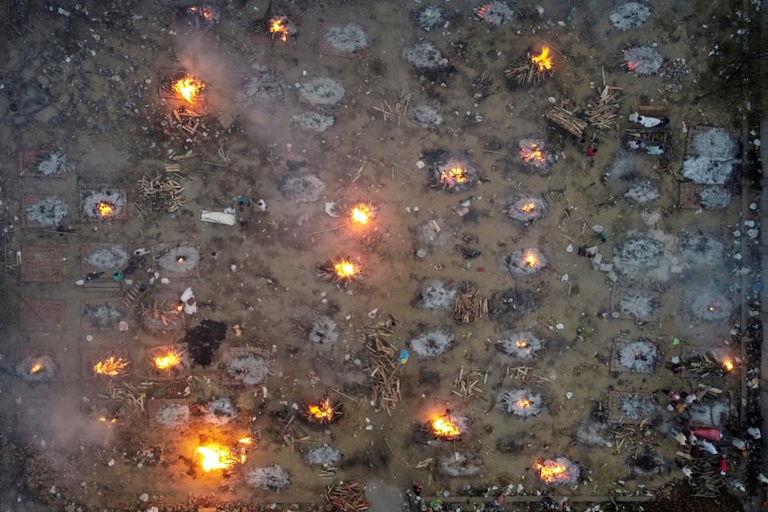 A mass cremation of victims is seen from above as spot fires across the ground.
