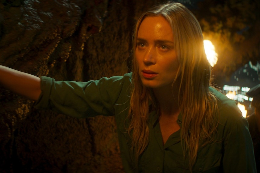 Emily Blunt looks worried as she walks up a hill at night, illuminated by torchlight