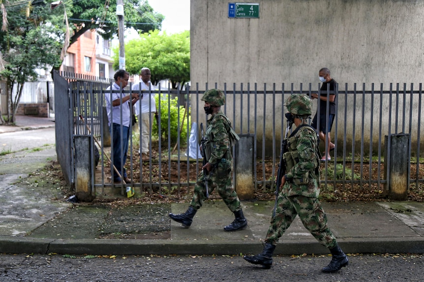 Two uniformed soldiers pass civilians on a street in Colombia