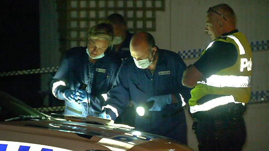 Three police officers gather around the bonnet of a police car and shine a torch on some documents.