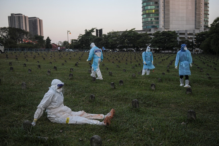 Health workers in PPE take a break while burying bodies of COVID-19 victims 