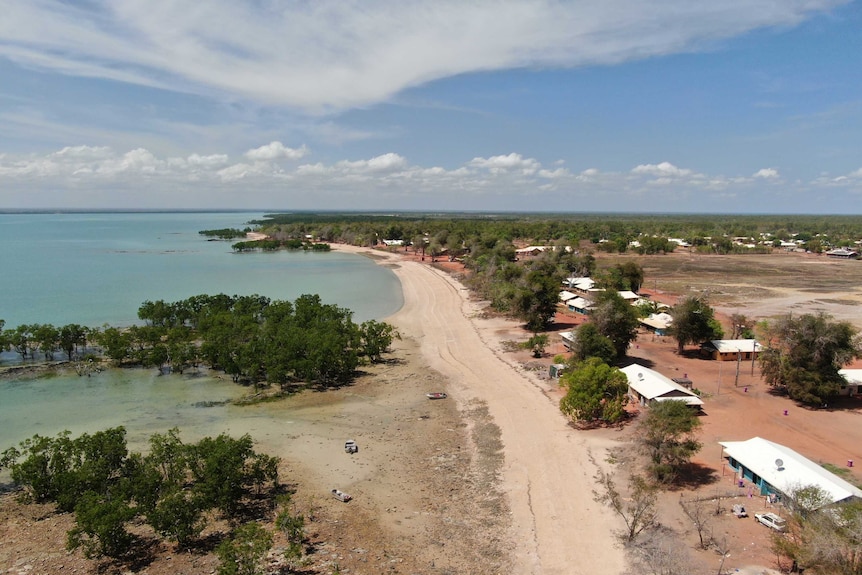 An aerial shot shows a sandy track leading to the beach. The rooves of houses are also visible