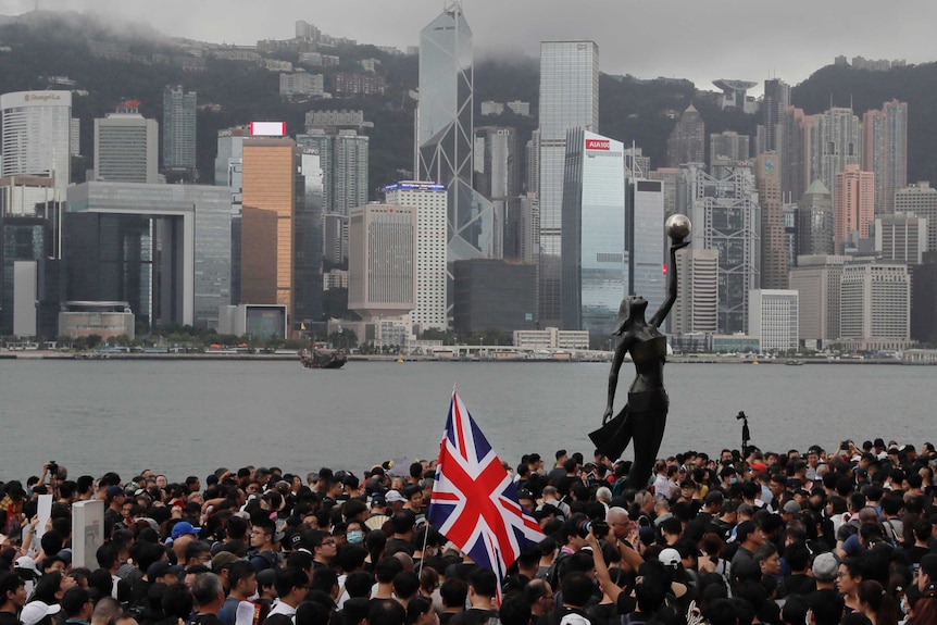La bandera del Reino Unido ondea en una multitud abarrotada cerca de un puerto con el horizonte de la ciudad detrás.