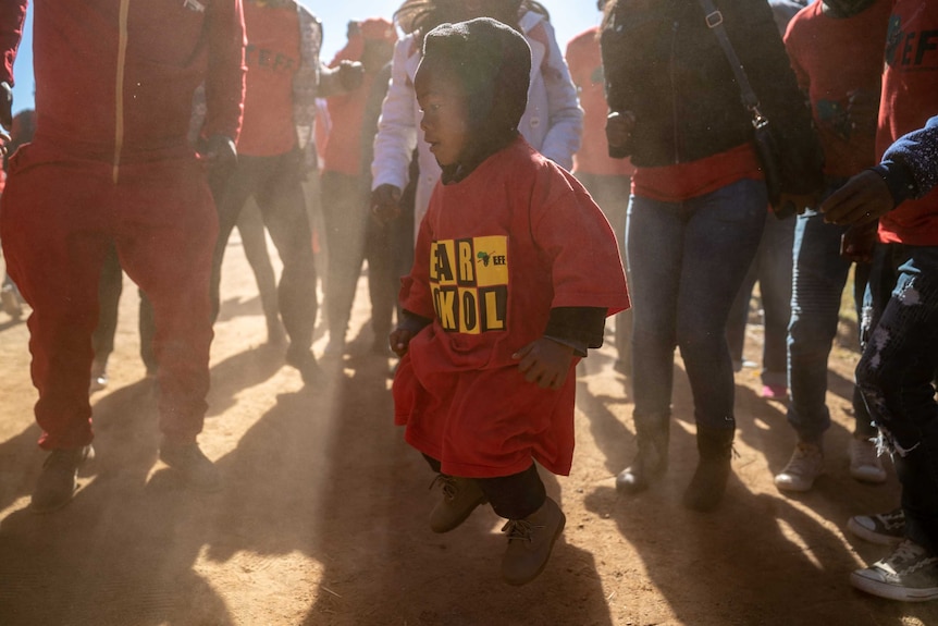A young boy joins the crowd at an EFF rally in an oversize red t-shirt.