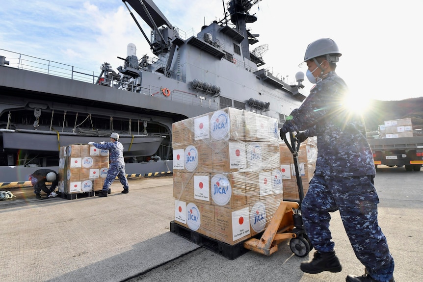Soldiers load emergency relief aid boxes onto a ship.