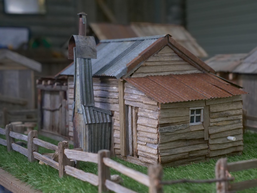 A model of a rustic country cabin, showing weather signs, a fireplace, a window and a fence.