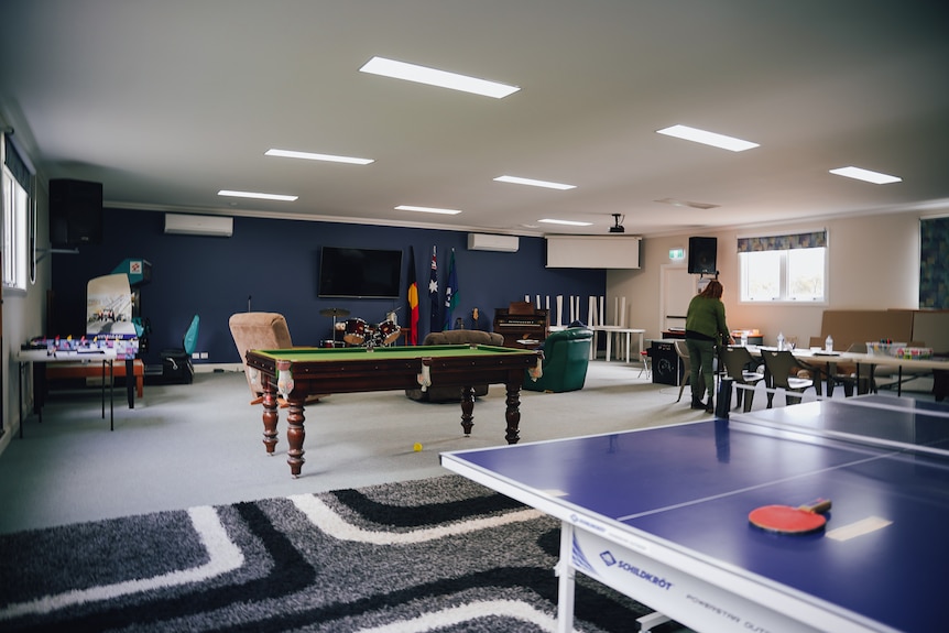 A pool table and billiards table sit in a large hall with a TV and other games.