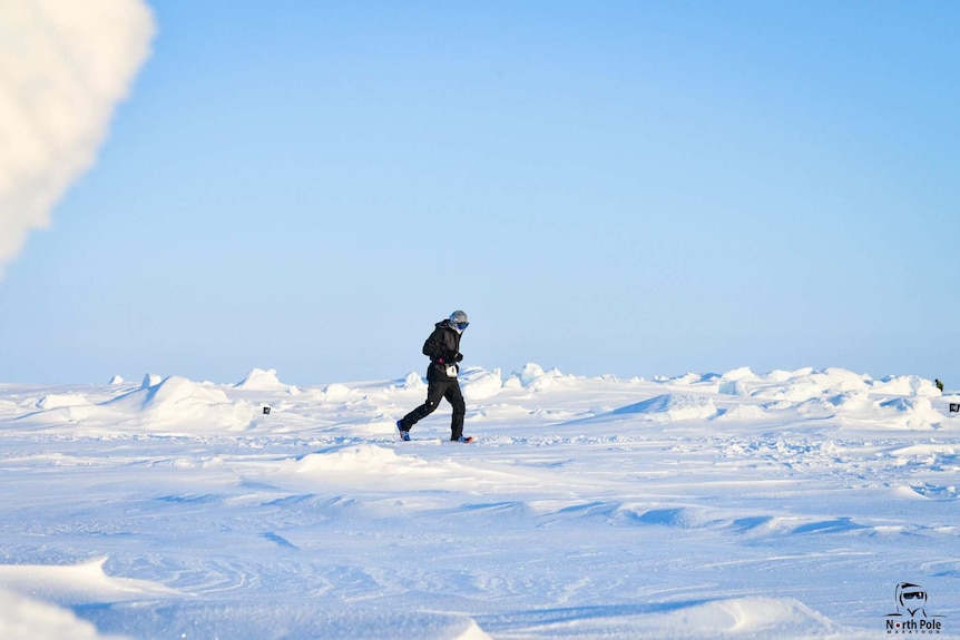 A man in protective winter clothing runs across a baron landscape of ice and snow.