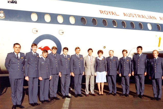 A line of RAAF officers with Prince Charles in the middle. They're standing on a tarmac with RAAF plane in the background.