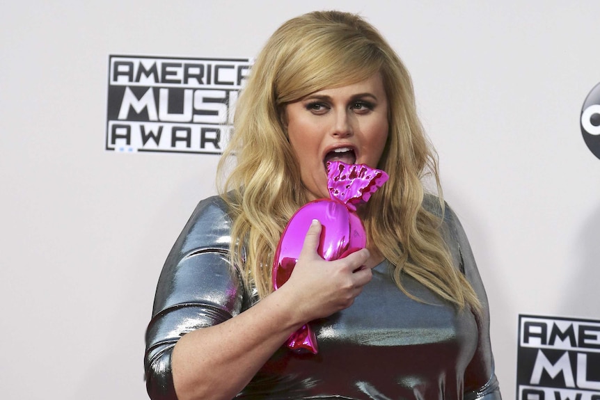 Rebel Wilson pretends to eat her lolly-shaped purse on the red carpet