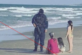 A dressed-in-black police office speaking with a mother and her children on the beach.