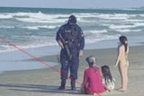 A dressed-in-black police office speaking with a mother and her children on the beach.
