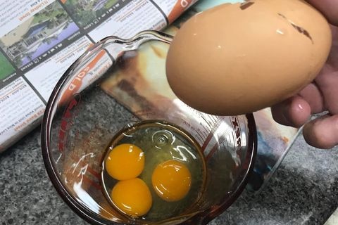 A long and large cracked egg is held above a glass measuring jug with three egg yolks in it.