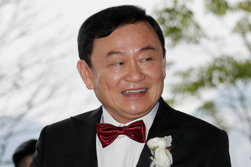 A man wearing a dark suit and red bow tie smiles over his shoulder.
