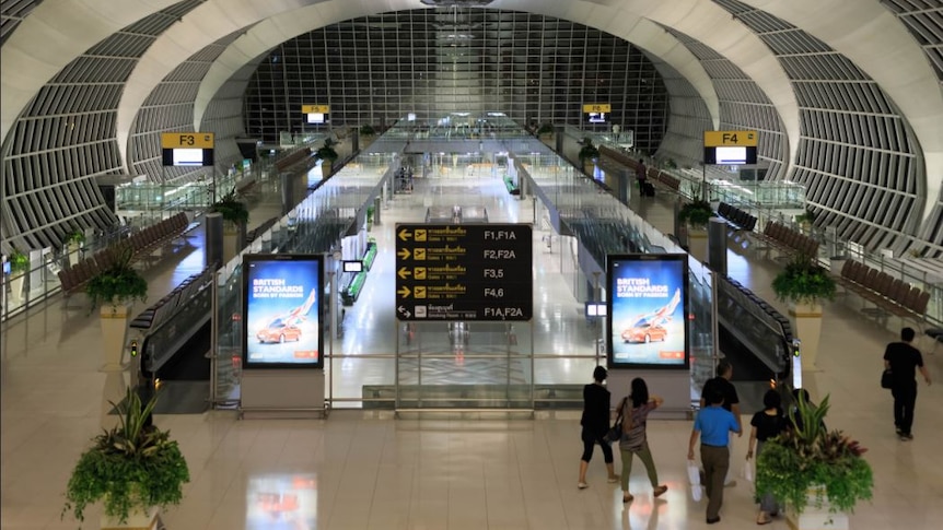 Photo of Suvarnabhumi International Airport terminal showing a sign between two parallel travelators, with passengers walking.