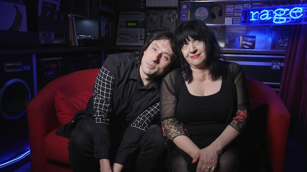 Two people wearing black clothing sitting on a red couch in the rage studio
