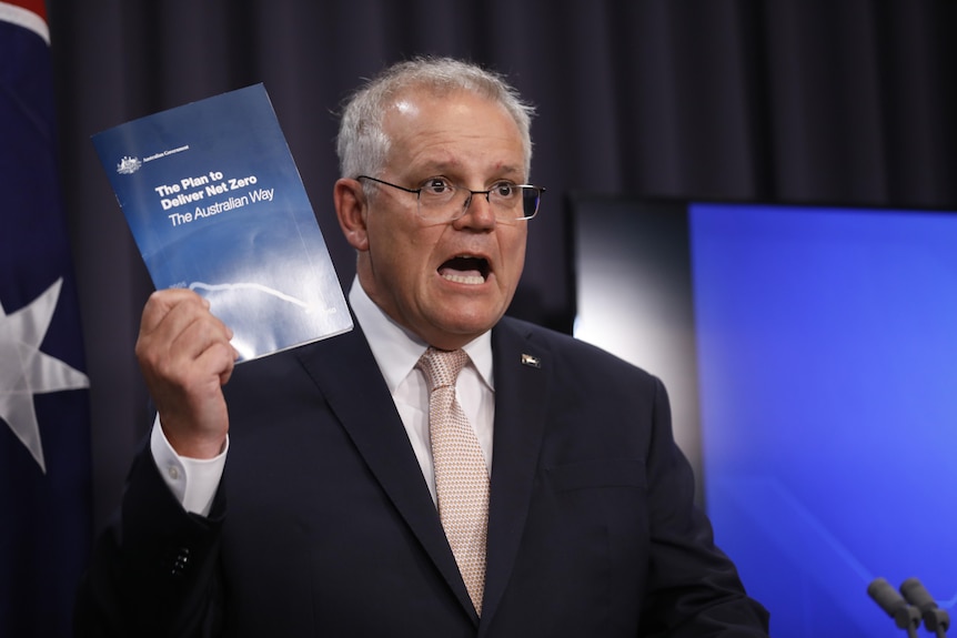 Scott Morrison talks while holding up a booklet reading "The Plan to Deliver Net Zero The Australian Way".