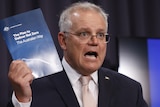 Scott Morrison talks while holding up a booklet reading "The Plan to Deliver Net Zero The Australian Way".