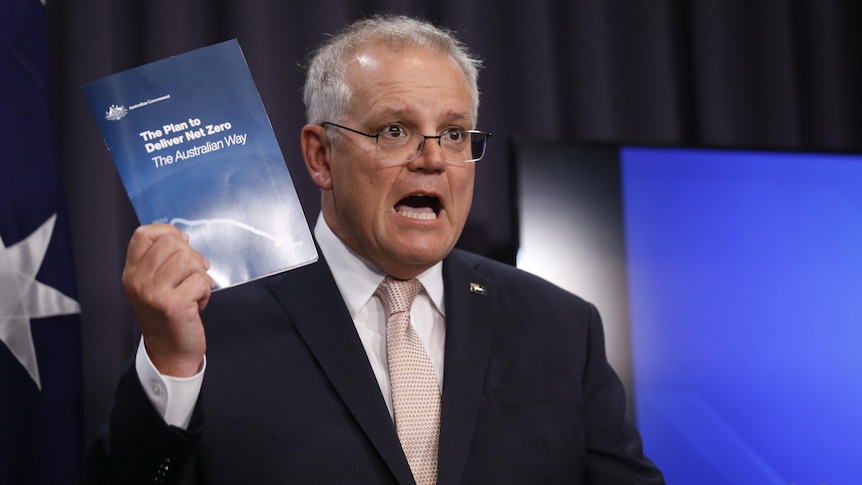 Scott Morrison talks while holding up a booklet reading "The Plan to Deliver Net Zero The Australian Way".