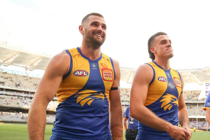 West Coast Eagles players Jack Darling and Jake Waterman walk off the ground looking happy after a win.