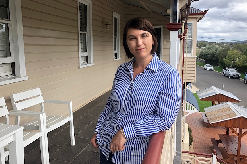 A woman wearing a blue and white striped shirt stands on the balcony of a country pub.