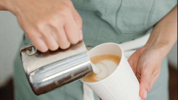 Womans hands pouring coffee from silver jug into white take away coffee cup